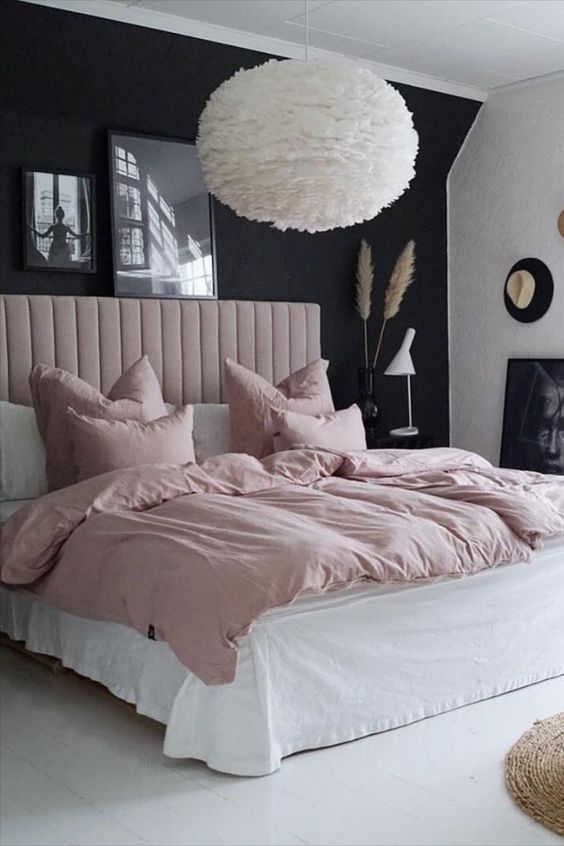 a beautiful and contrasting bedroom with a black accent wall, a blush upholstered bed and blush bedding, a fluffy pendant lamp and a mini gallery wall