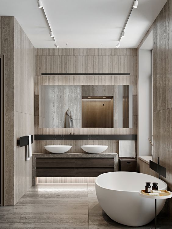 A beautiful bathroom clad with wood imitating tiles, an oval tub and matching sinks, a large mirror and built in lights
