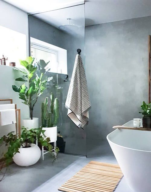 A beautiful bathroom done with concrete, an oval tub, potted plants and a towel stand is a chic and cool space