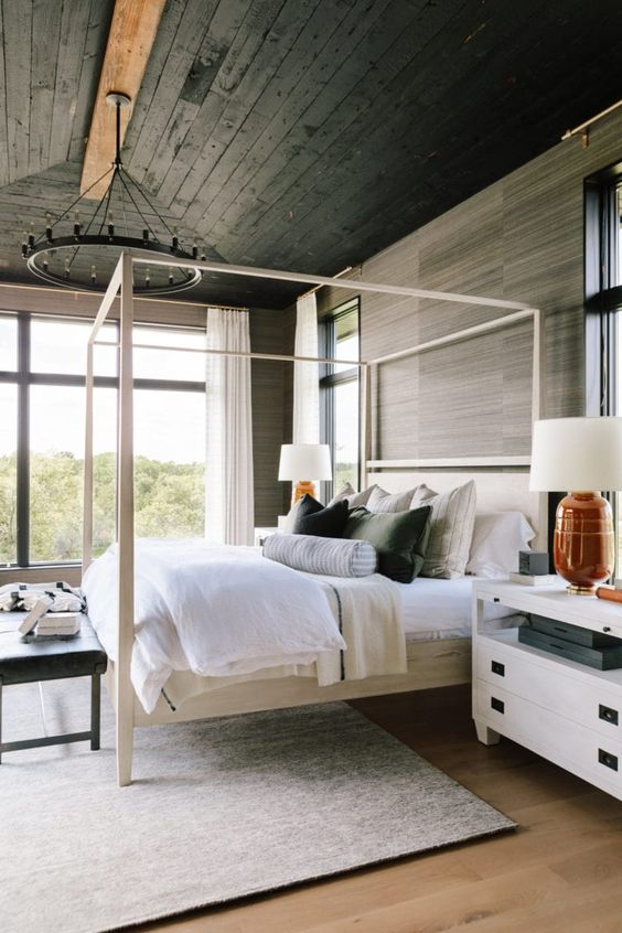 a beautiful bedroom with a black planked ceiling and wood-inspired wallpaper, a neutral canopy bed, white nightstands and creative bedding