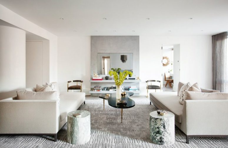 a beautiful contemporary living room with floating shelves and a mirror, creamy sofas, stone side tables, a catchy coffee table and lots of accessories