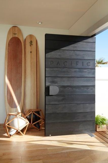 a black stained wooden pivot door with a metal knob is a gorgeous idea for many spaces and adds a beach feel with the inscription