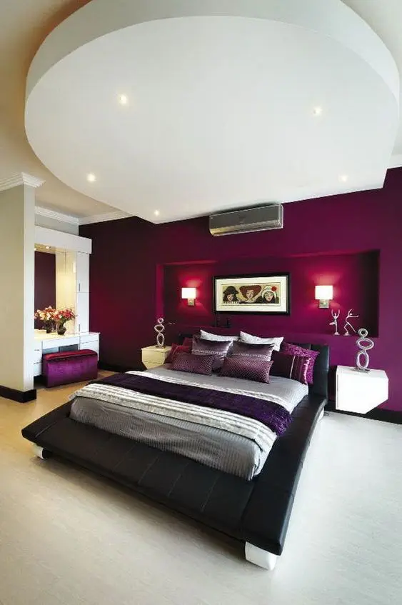 a bold and refined bedroom with a purple accent wall with a niche for lamps, a black bed, a chic vanity space and built-in lights