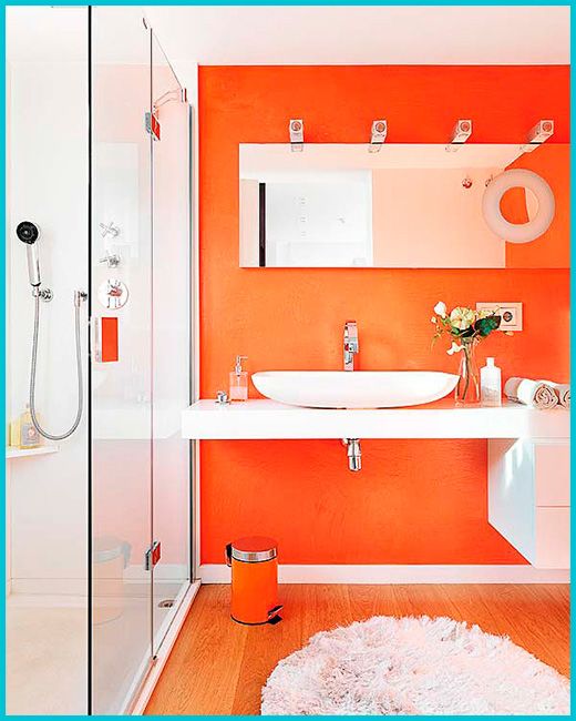 a bright bathroom with an orange accent wall and all white everything, with an orange trash can and a long mirror is wow