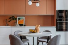 a bright contemporary kitchen with orange and white sleek cabinets, an orange backsplash and white countertops, a geo tile floor