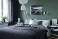a chic bedroom with a green accent wall, a bed and cool bent nightstands, a pendant lamp and a bold artwork plus moody bedding