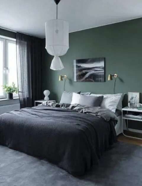 a chic bedroom with a green accent wall, a bed and cool bent nightstands, a pendant lamp and a bold artwork plus moody bedding