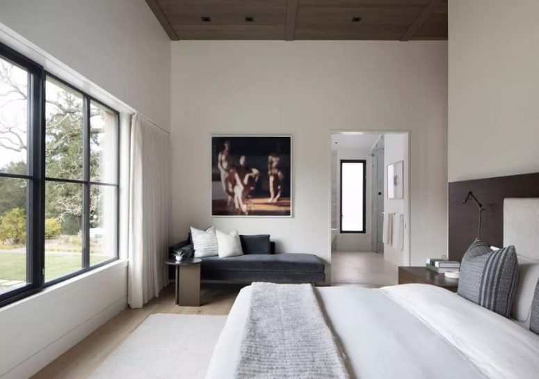 a chic contemporary bedroom with a wooden ceiling, a neutral upholstered bed with neutral bedding, a graphite grey upholstered daybed and a small side table plus a lovely artwork