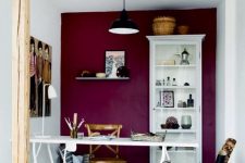 a chic craft room with a purple accent wall, white furniture, baskets with posters and artworks and a black pendant lamp plus a wooden beam