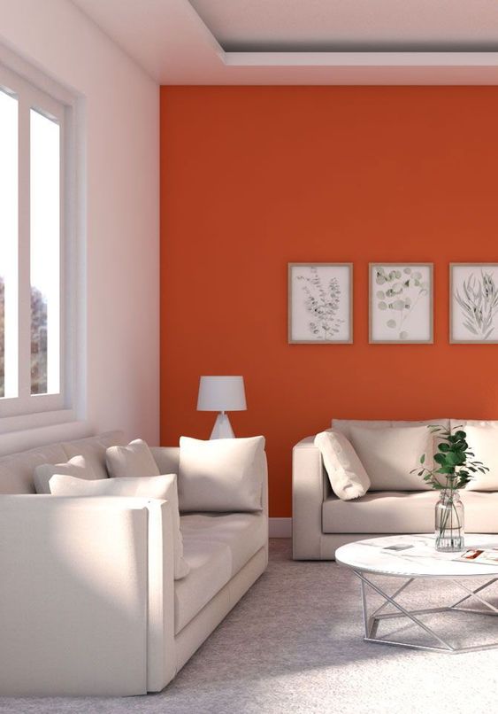 a chic modern living room with an orange accent wall that sets up the mood, neutral sofas, a cool table and a mini botanical gallery wall