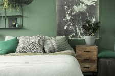 a chic organic bedroom with a green accent wall, a bed, a shabby chic nightstand, a woven pendant lamp and a chic floral artwork
