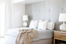 a clean neutral contemporary bedroom with a grey upholstered wall and an upholstered bed that matches, neutral textiles and a large rug