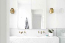 a clean white bathroom with a large mirror, a large floating vanity clad with marble and tiles and brass fixtures is cool