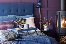 a colorful bedroom with deep purple panel walls, a blue bed and blue bedding, a hearth and a lamp on a branch