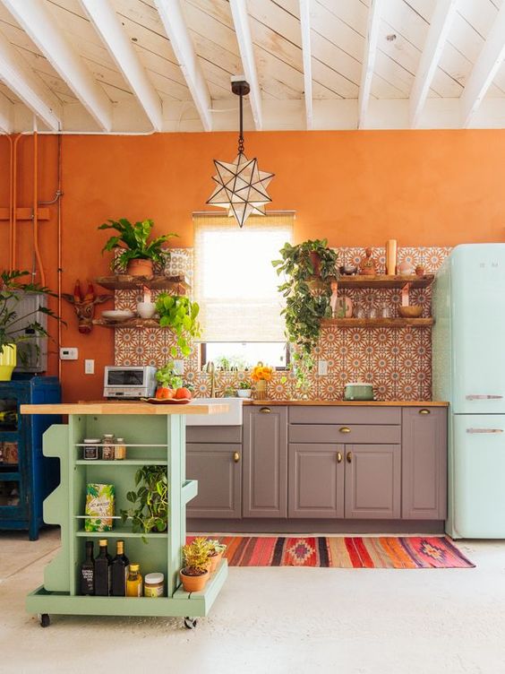 a colorful kitchen with an orange accent wall, a bright mosaic tile backsplash, grey cabinets, a blue fridge and a green cart kitchen island