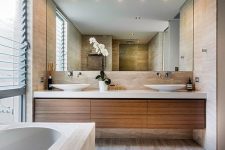a contemporary bathroom clad with neutral stone-imitating tiles, a floating vanity, a large mirror, a glazed wall with shades