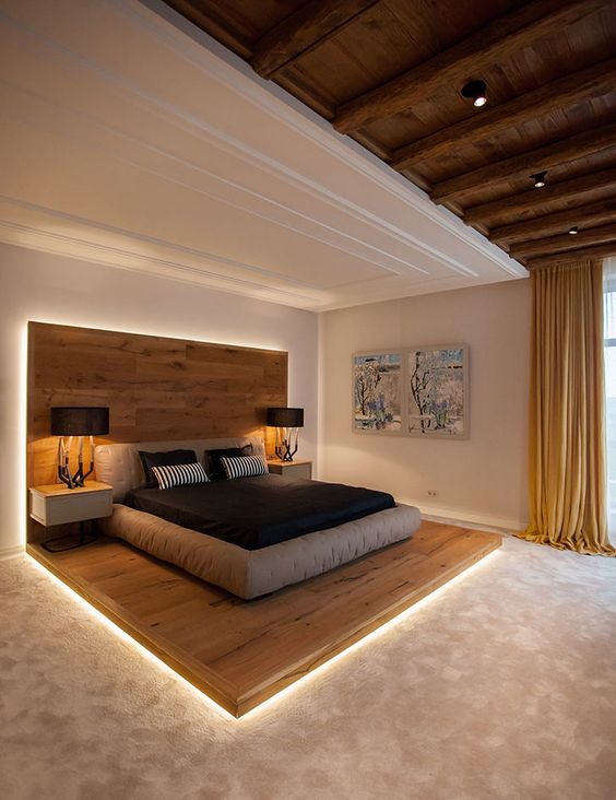 a contemporary chalet-inspired bedroom with a bed on a wooden platform that has an extended headboard, a grey upholstered bed and floating nightstands plus built-in lights