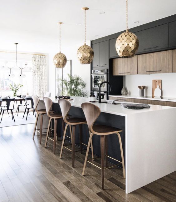 a contemporary kitchen with stained and black cabinets, a black kitchen island, white countertops and a backsplash, gold scale pendant lamps