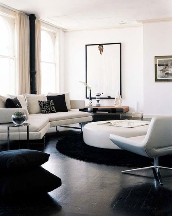 a contemporary living room in black and white, with a black floor, chic white furniture, a round table, a statement artwork and printed pillows