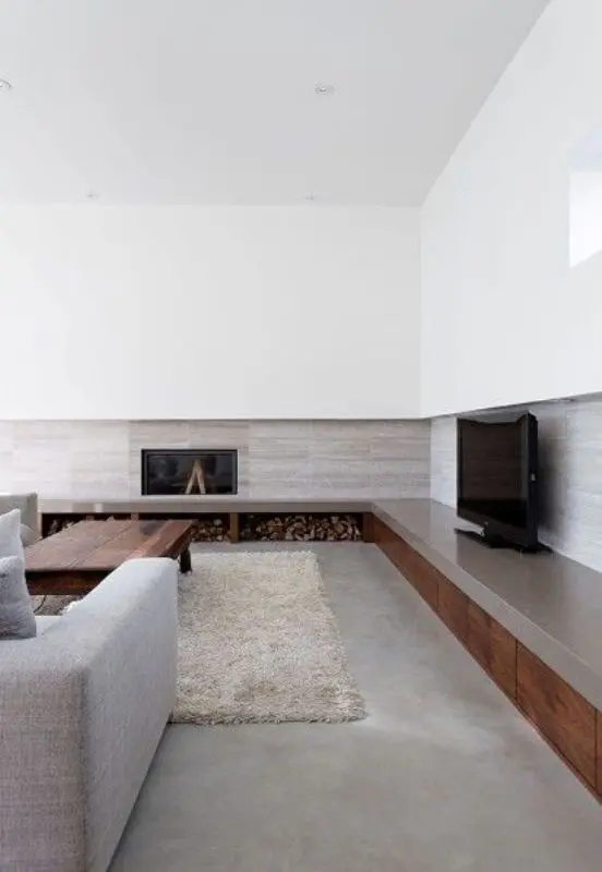 a contemporary living room with a concrete floor, paneled walls, a built-in fireplace and firewood storage, grey seating furniture and a stained table