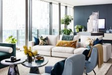 a contemporary living room with splashes of color, a grey wall, a glazed one, muted and jewel tone seating furniture, stone coffee tables and printed pillows