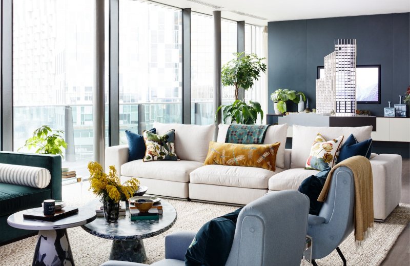 A contemporary living room with splashes of color, a grey wall, a glazed one, muted and jewel tone seating furniture, stone coffee tables and printed pillows