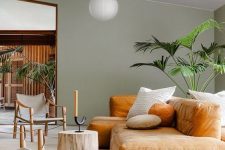 a contemporary living space with an amber-colored low sofa, a tree sutmp, catchy wooden chairs, statement plants and pendant lamps