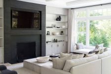 a cozy black and white contemporary living room with a built-in TV and fireplace, open shelves, a cabinet, a neutral sofa and daybed, a low table and a black chair