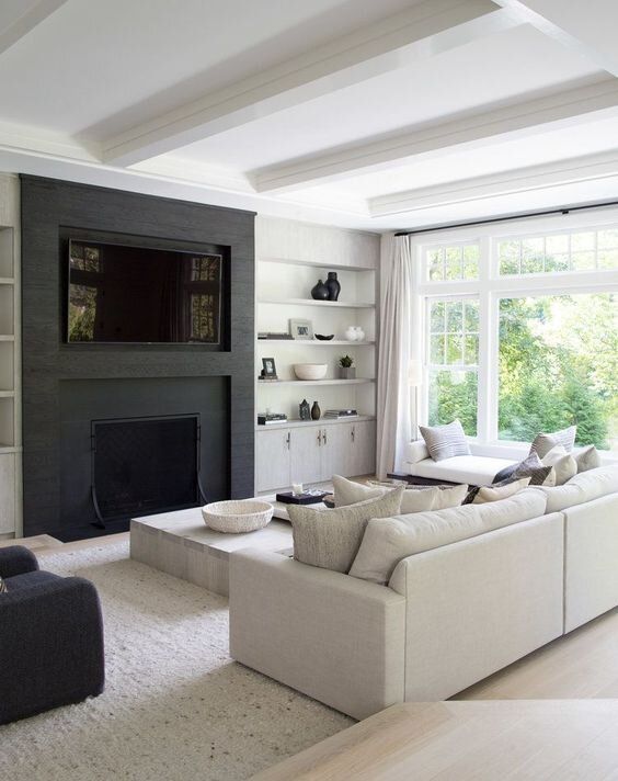 A cozy black and white contemporary living room with a built in TV and fireplace, open shelves, a cabinet, a neutral sofa and daybed, a low table and a black chair