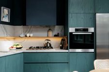 a fantastic teal kitchen that shows off grains of wood, a navy hood that merges with the wall, a white stone backsplash and countertop