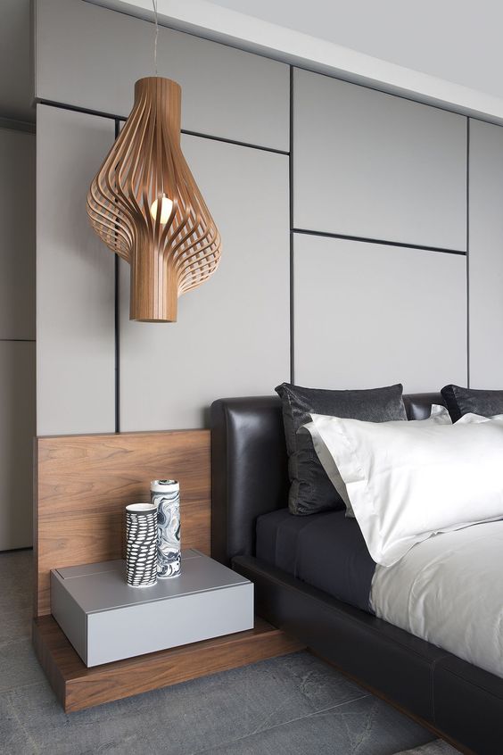 A gorgeous contemporary bedroom with a grey panel accent wall, a black leather bed, contrasting bedding, a floating nightstand and a jaw dropping pendant lamp