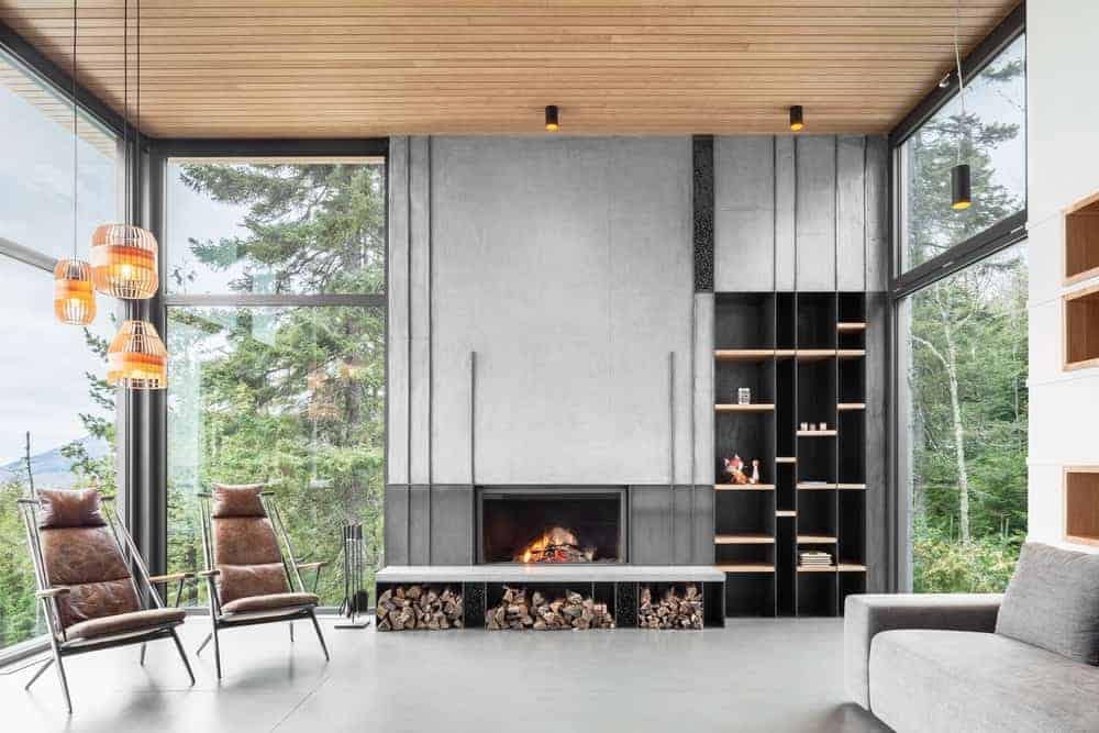 A gorgeous contemporary living room with a view, a built in fireplace and firewood storage, a grey sofa, leather chairs, pendant lamps