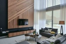 a gorgeous contemporary living room with a wood clad accent wall, a TV, grey furniture, side and coffee tables and double-height windows