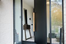 a heavy black metal pivot door with a long light-stained handle is a cool idea for making and statement with style