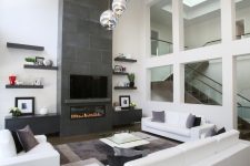 a laconic contemporary living room with a fireplace clad with tiles, white sofas and a chair, a tiered glass coffee table and open shelves