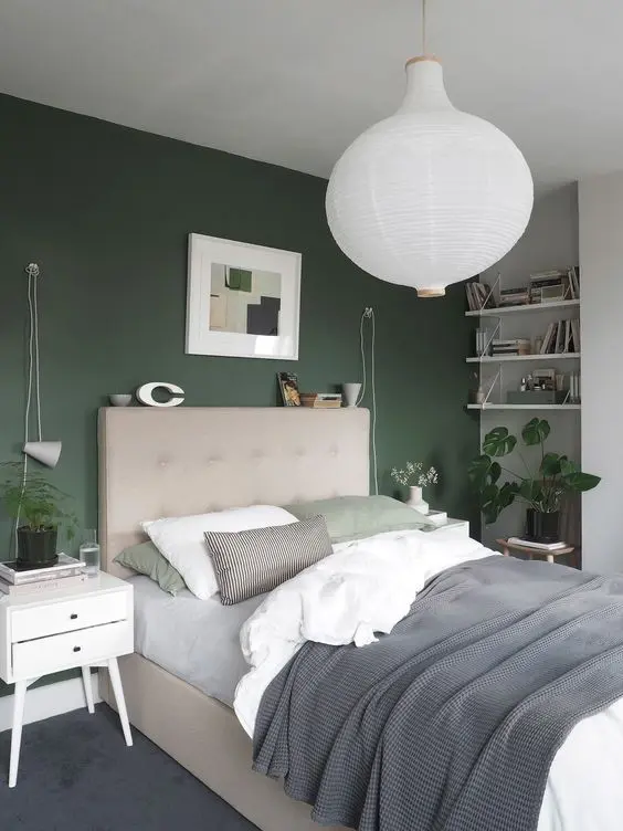 a lovely Scandinavian bedroom with a green accent wall, a tan upholstered bed, white nightstands and shelves, a pendant lamp and neutral bedding