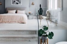 a lovely bedroom with a grey accent wall, a grey upholstered bed, pink bedding, pendant lamps, a potted cactus and a statement artwork