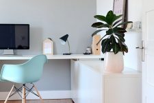 a lovely contemporary home office with a sleek storage unit and a built-in desk, a mint blue chair, potted greenery and a cool clock