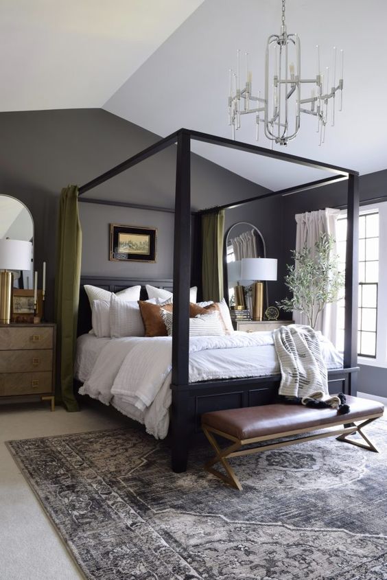 a lovely master bedroom with grey walls, a black canopy bed, neutral bedding, green curtains, a modern chandelier and a leather bench