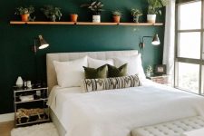 a lovely mid-century modern bedroom with a green accent wall, a creamy upholstered bed and a bench, a shelf with potted greenery