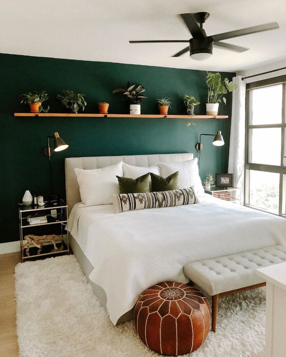 A lovely mid century modern bedroom with a green accent wall, a creamy upholstered bed and a bench, a shelf with potted greenery