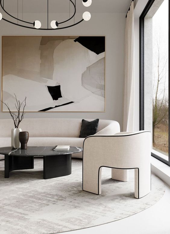 a luxurious contemporary living room in neutrals and black, with a curved sofa and a chair on three legs, a black marble table, a chandelier plus a statement artwork