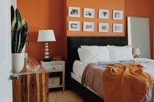 a mid-century modern bedroom with an orange accent wall, a black bed and neutral nightstands, a reclaimed wood dresser and a small gallery wall