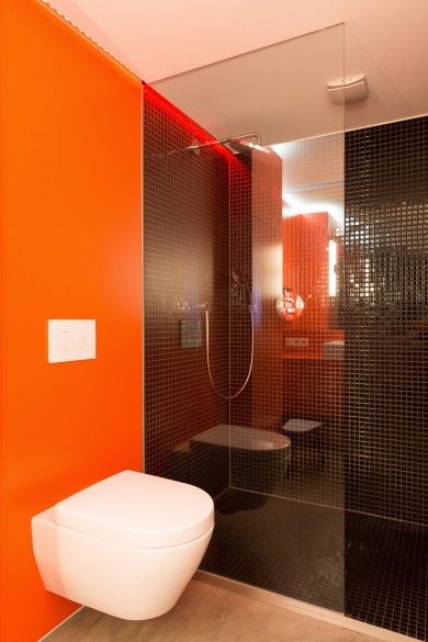 A minimalist bathroom with an orange accent wall, a shower space clad with black tiles is a very chic and cool space