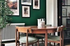 a modern dining nook with an emerald accent wall, a bright gallery wall, a round table and cool green chairs, a potted tree plus a graphic rug