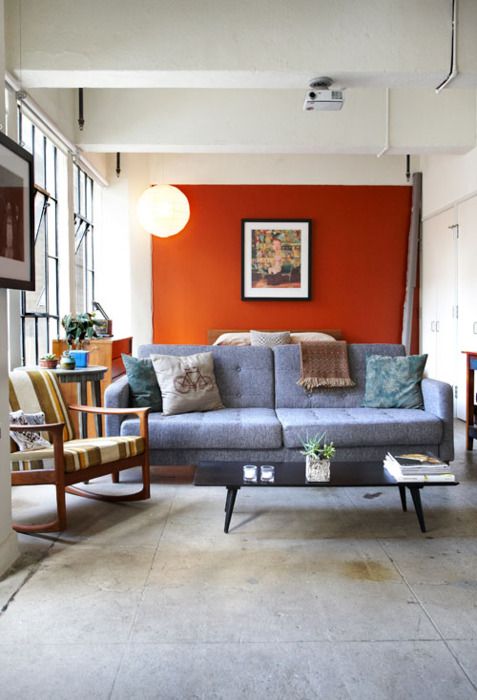 a modern living room with an orange accent wall, a grey sofa, a striped chair, a low coffee table and some bold artworks
