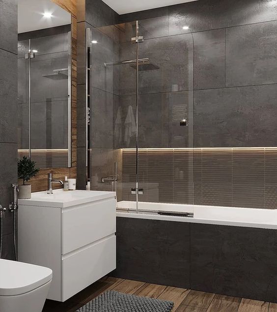 a moody contemporary bathroom clad with dark stone tiles, with built-in lights, a wooden floor, white appliances and neutral fixtures