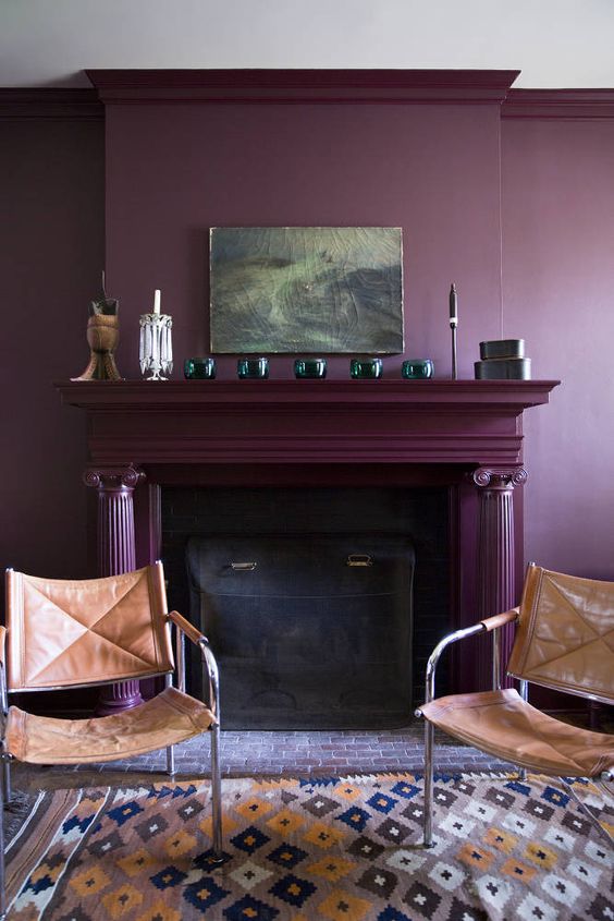 a moody living room with a deep purple accent wall, a fireplace done in the same color, leather chairs and some decor on the mantel
