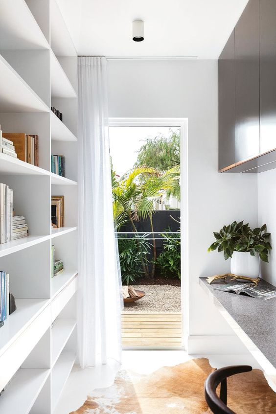 a narrow contemporary home office with an oversized white shelving unit, a floating desk and dark storage cabinets