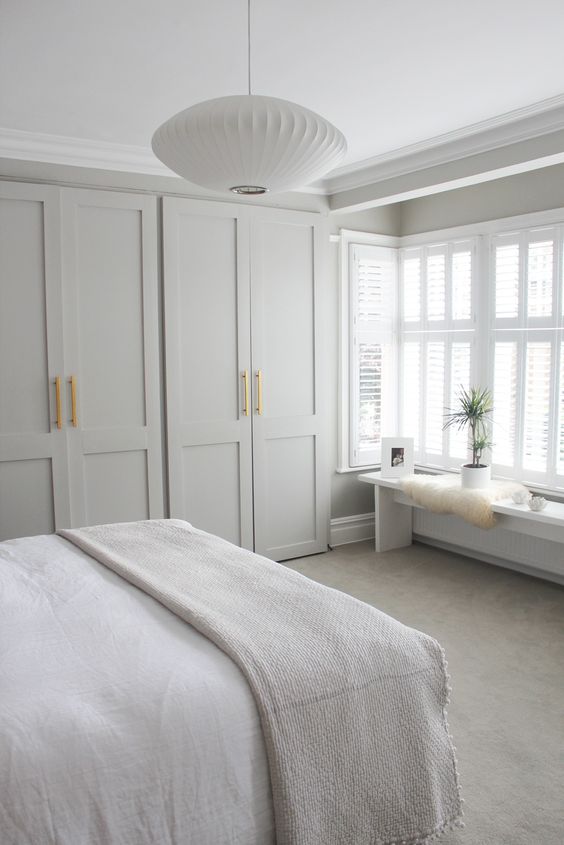 a neutral Zen bedroom with a large closet with shaker style doors, a bench with a potted plant and some artworks and a pendant lamp